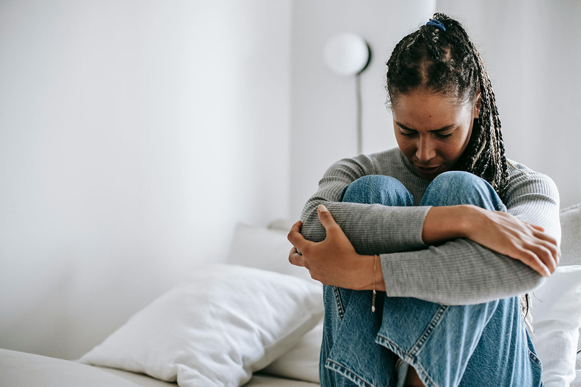 Woman with anxiety sitting on bed with her arms around her legs
